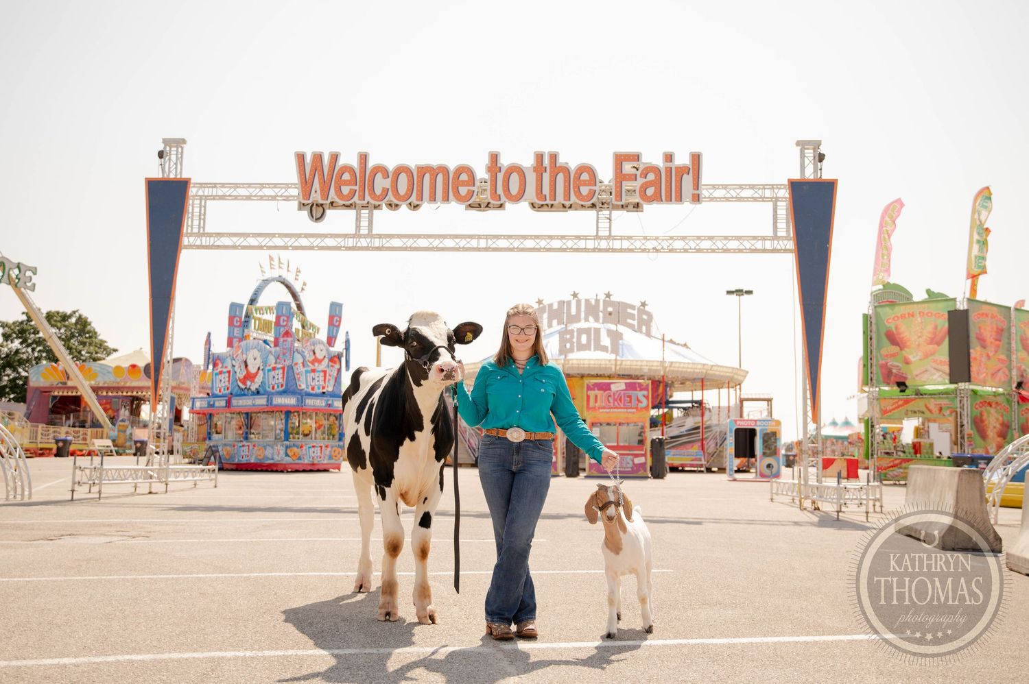 Woman leads a Holstein cow and small goat at a colorful county fair with vendor booths and Weis Markets sign.