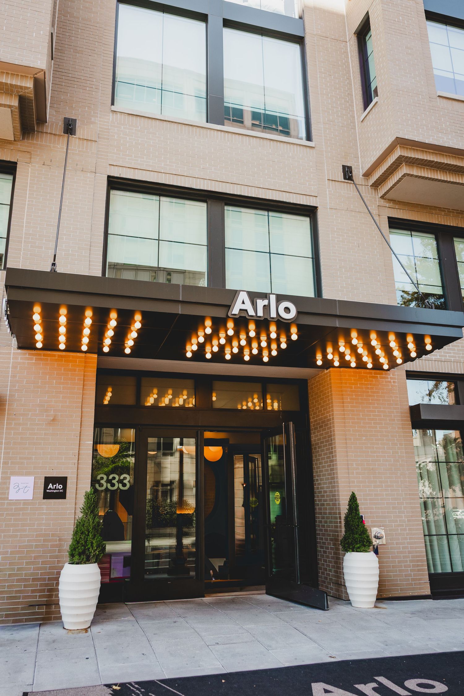 Arlo hotel entrance at 333 with illuminated marquee lights above glass doors flanked by white planters.