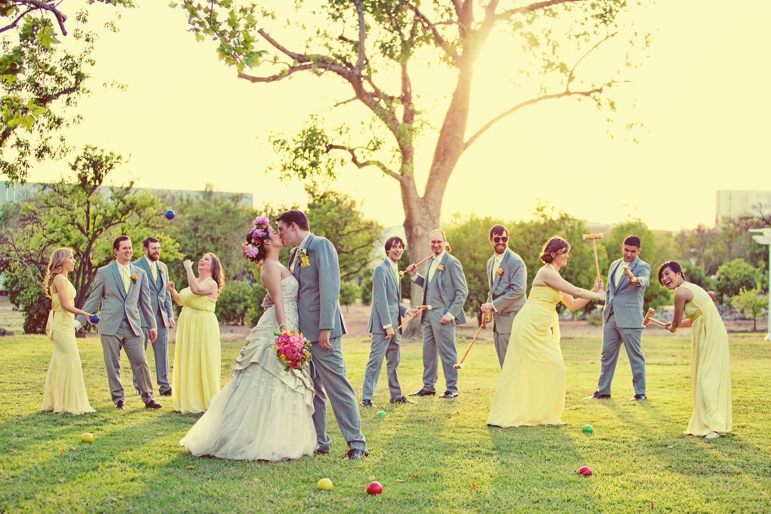 Wedding party in yellow dresses and gray suits posing outdoors under a tree on a sunny day.