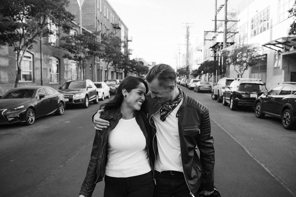 Black and white photo of a couple walking and embracing on a city street, smiling at each other.