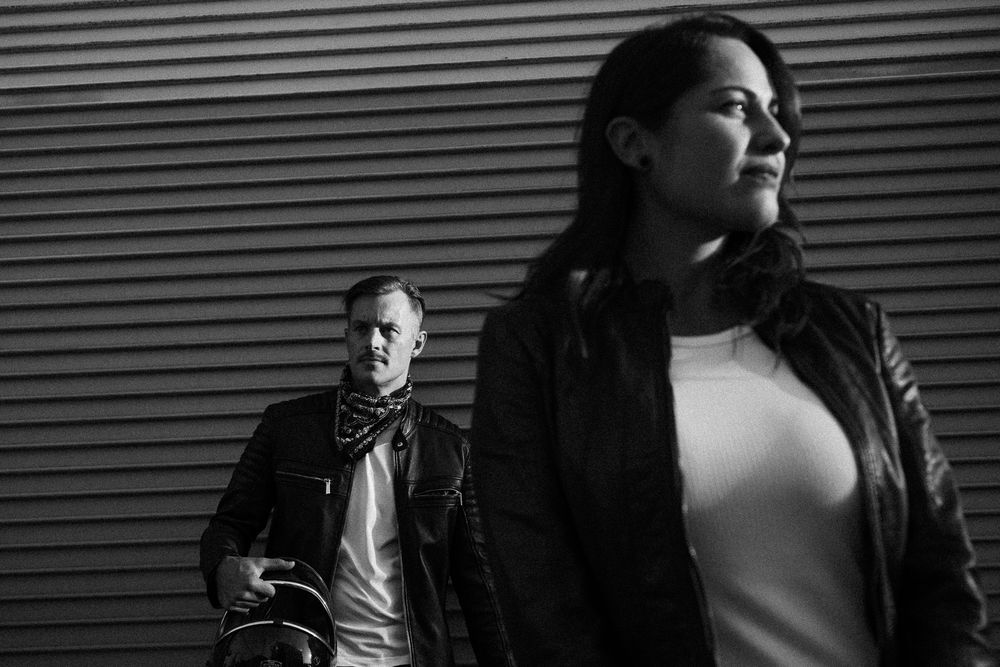 Black and white photo of couple in leather jackets with moody urban background.