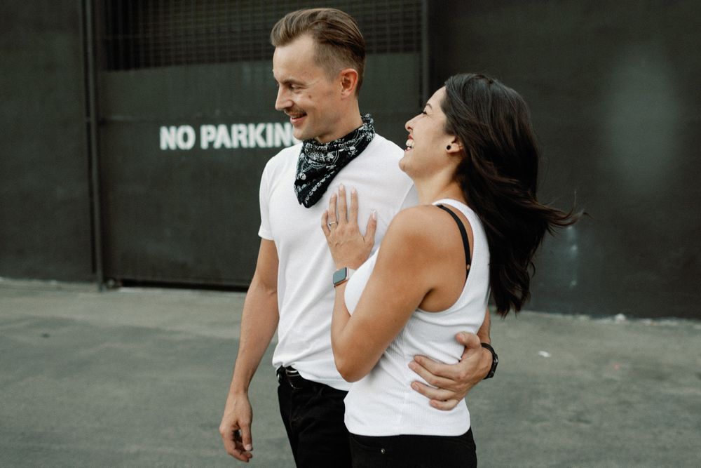 A smiling couple embraces while walking, the man wearing a bandana and the woman in a white tank top.