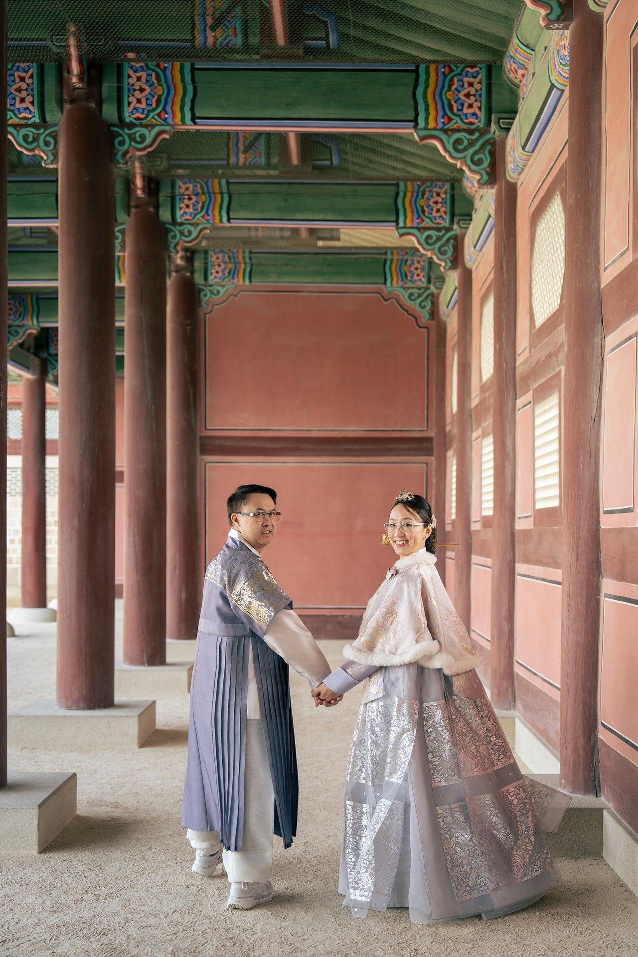 Couple in traditional Korean hanbok holding hands in a colorful palace corridor at Gyeongbokgung, Seoul.