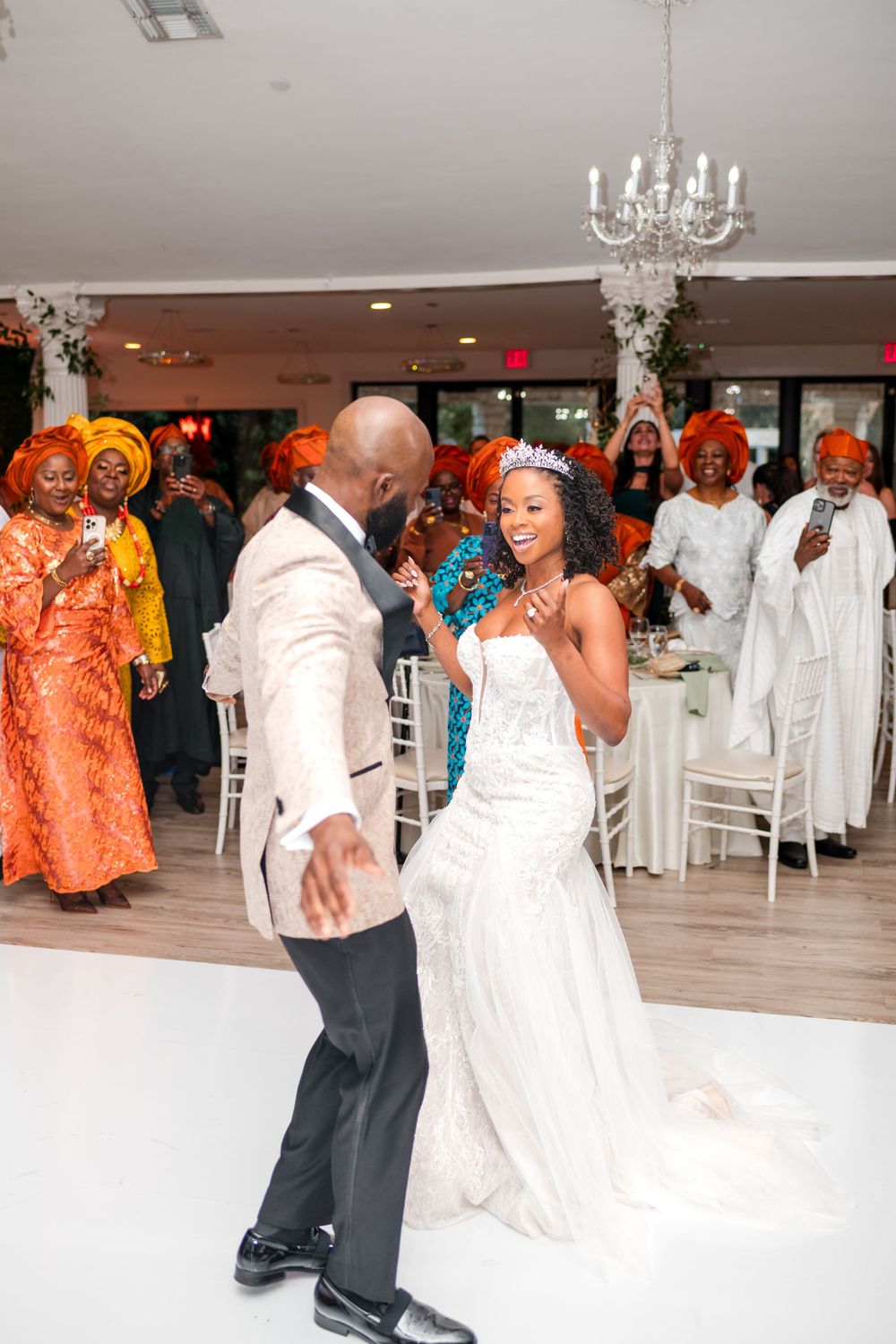 Guests dance and celebrate at a wedding reception with orange and white color scheme decor and formal attire.