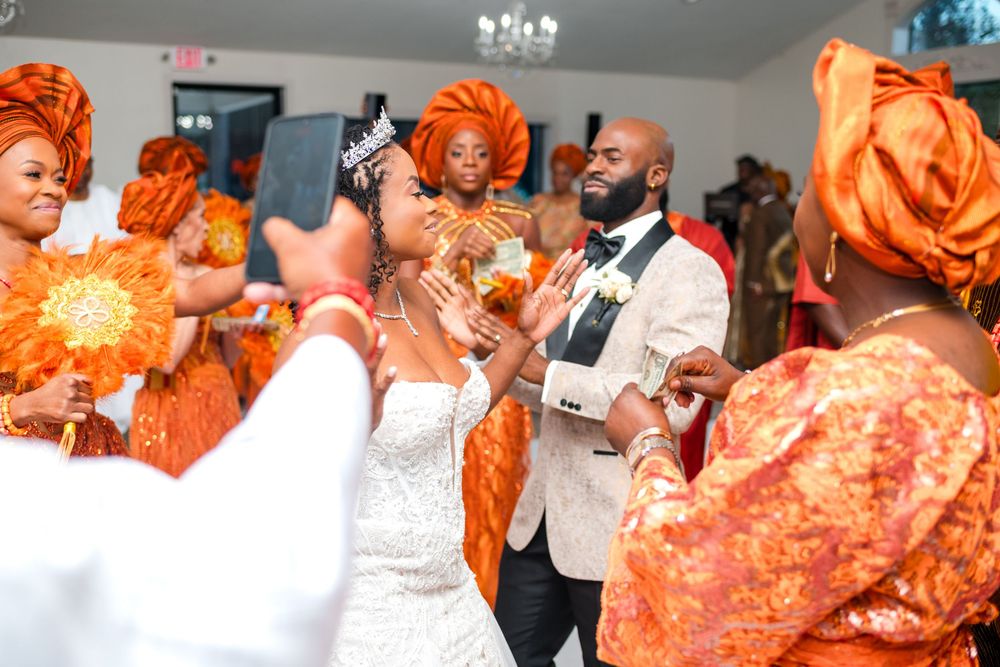 A wedding celebration features guests in vibrant orange and white traditional attire dancing and celebrating together.