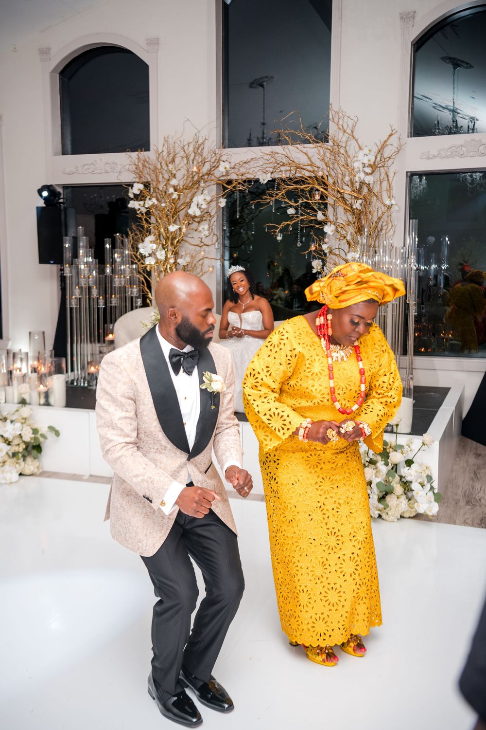 Wedding guests dance and celebrate in a bright reception hall with modern white decor and branch arrangements.