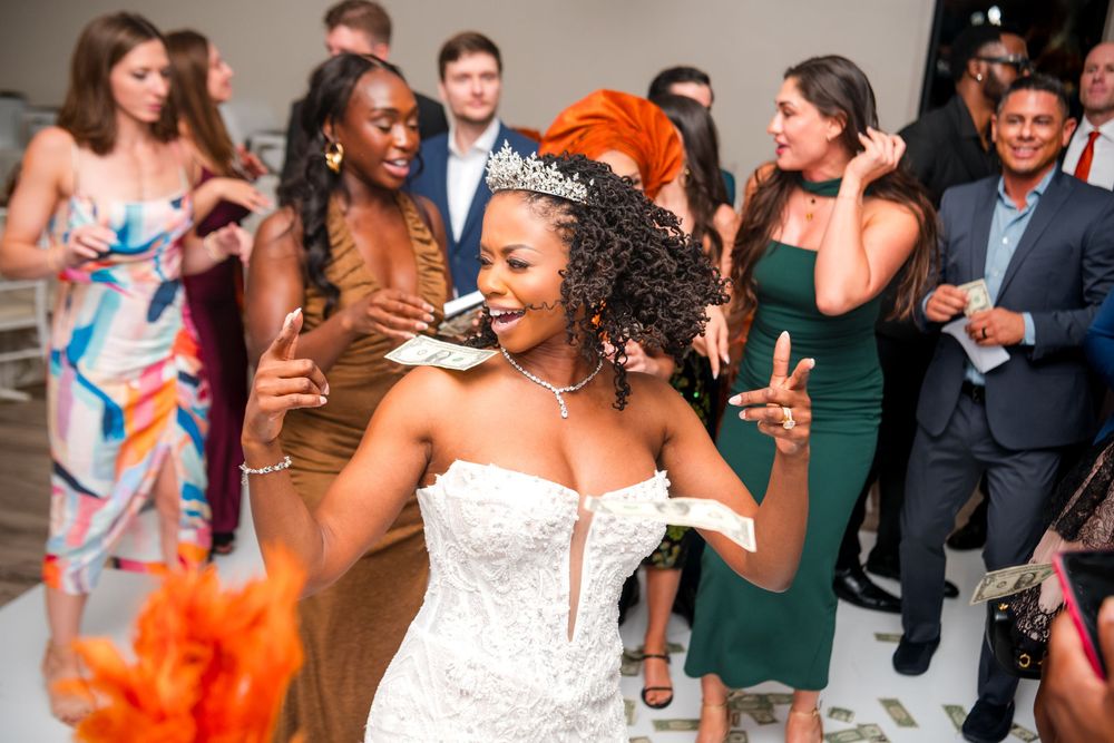 Bride in white strapless dress dances joyfully at wedding reception while wearing vibrant orange feather accessories.