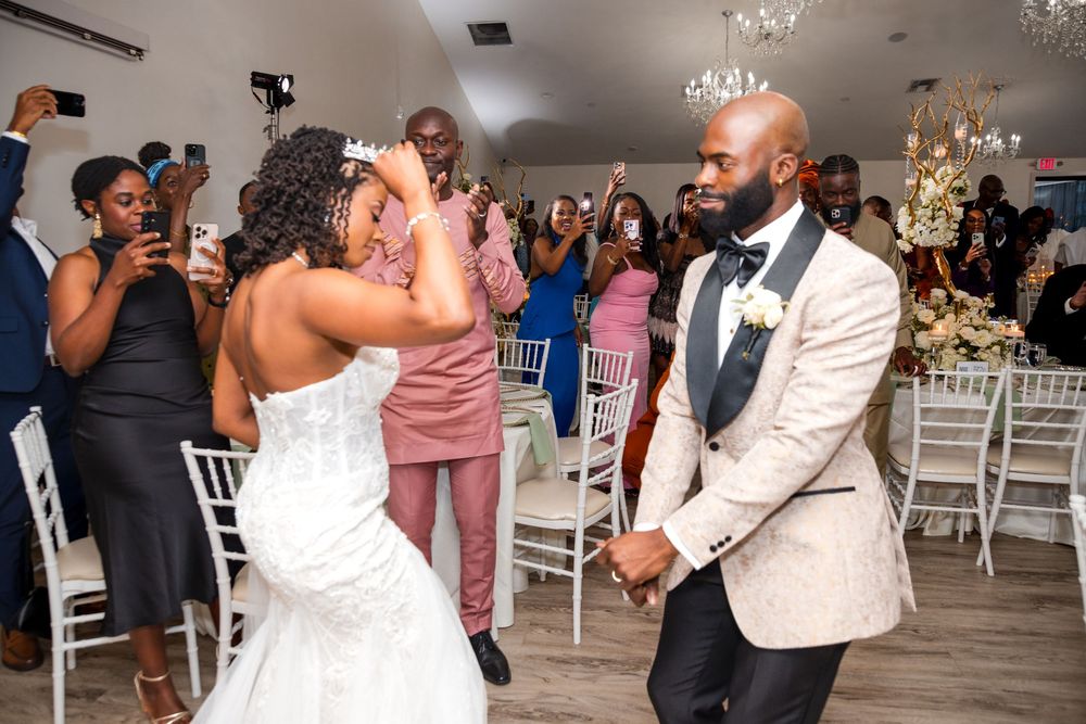 Wedding couple dancing together at their reception surrounded by guests in an elegant venue with chandeliers.