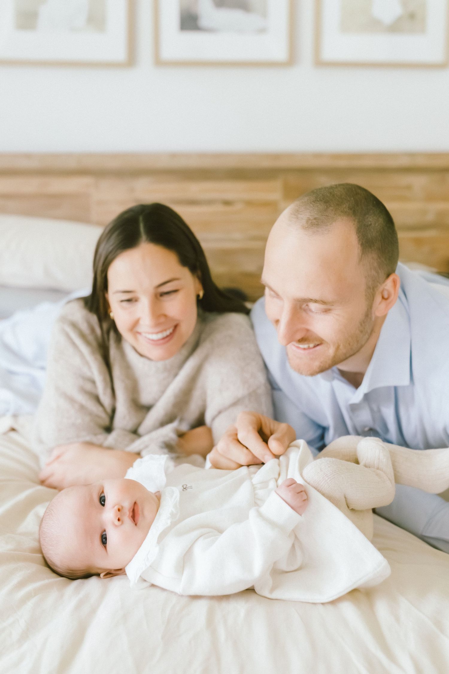 Happy parents lying on bed smiling at their newborn baby dressed in white during an in-home family photo session.