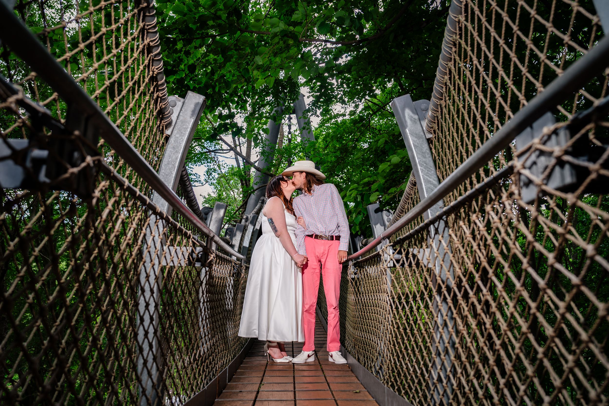Couple sharing a romantic moment on a suspended bridge walkway surrounded by lush green trees.