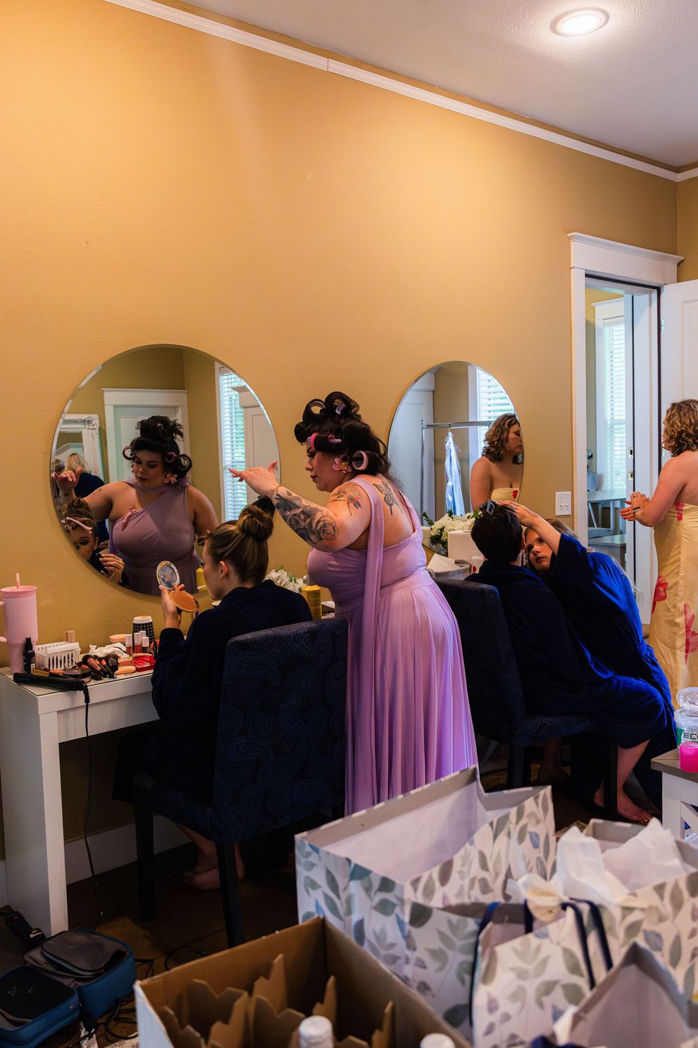 Bridesmaids getting ready in a dressing room with round mirrors and vanity lights before a wedding.