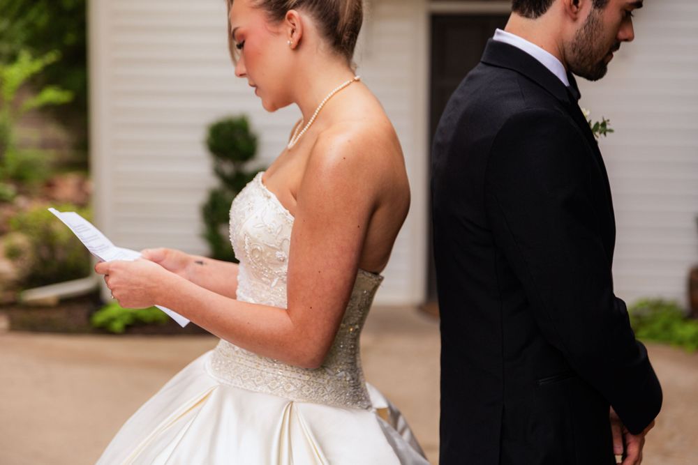 Bride in strapless beaded wedding gown reading a heartfelt letter during a first look moment.