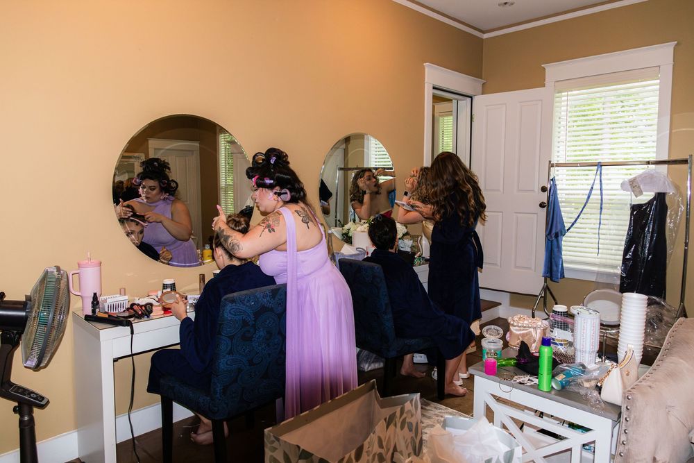 Bridesmaids in colorful gowns getting hair and makeup done in wedding preparation room.