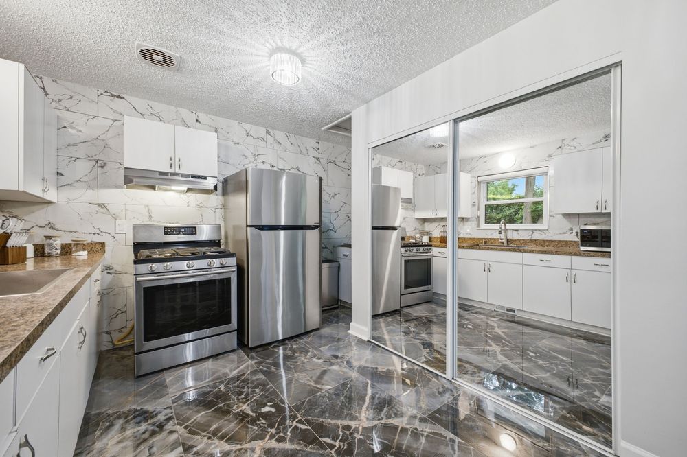 Modern kitchen with marble walls, dark marble floors, stainless steel appliances, and white cabinets with mirrored closet doors.