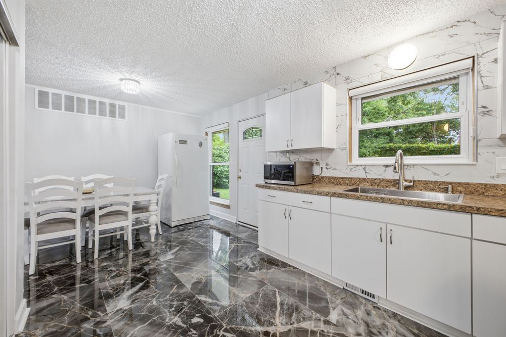 White kitchen with marble floors, white cabinets, granite countertops, and a dining area with natural light from windows.
