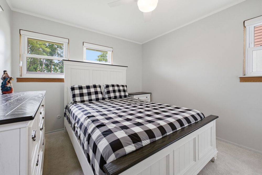 Cozy bedroom with black and white checkered bedding, white furniture, carpeted floors, and natural light from two windows.