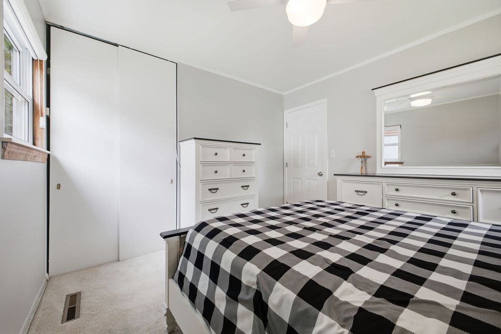 Bedroom with black and white checkered bedding, white dresser, closet, and mirror on light gray walls.