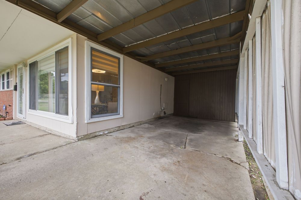 Covered carport with concrete flooring adjacent to a home exterior featuring white siding and a window.