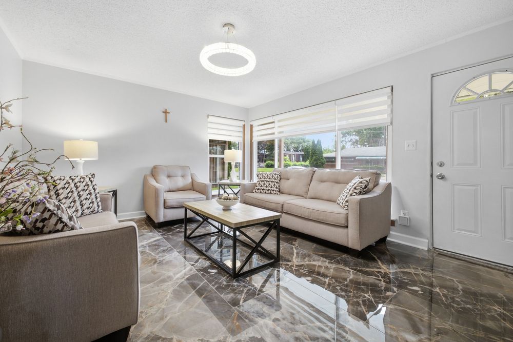 Modern living room with beige sofa, marble floors, black coffee table, and bright natural light from large windows.