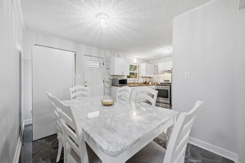 Bright white dining room with marble table and chairs opens to a modern kitchen with stainless steel appliances.