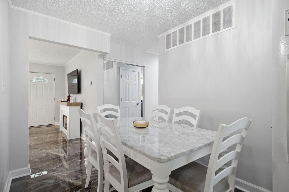 White dining room with marble-top table, ladder-back chairs, hardwood floors, and open view to entryway.