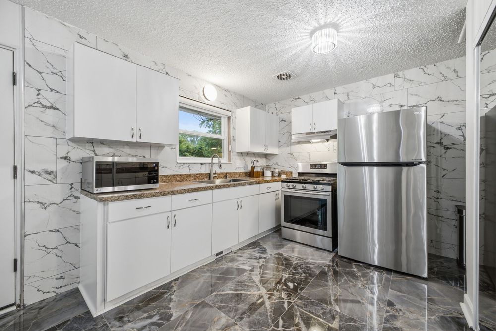 Modern kitchen with white cabinets, marble walls, stainless steel appliances, and dark marble floors.
