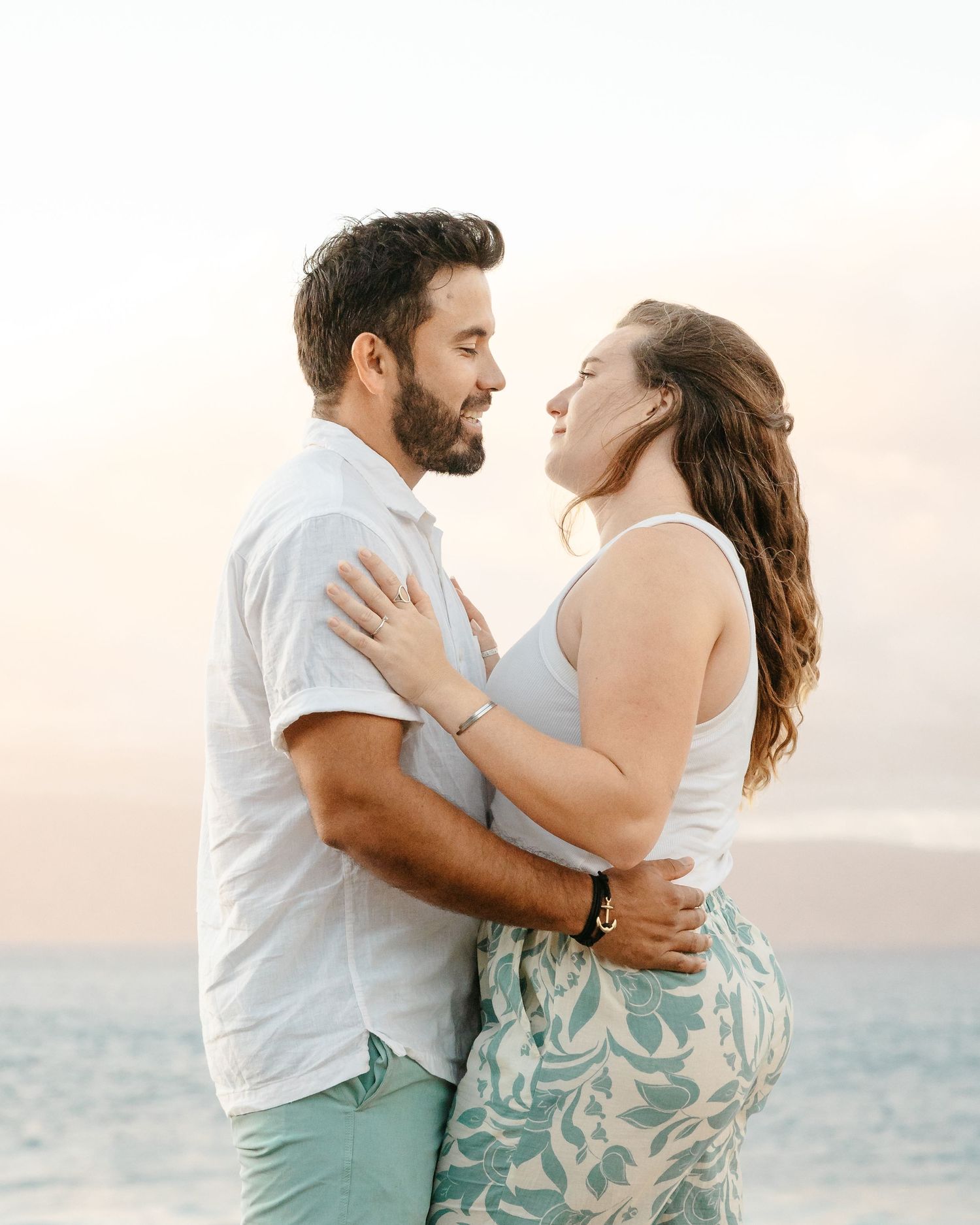 Loving couple embraces face to face on beach during soft pastel sunset light.