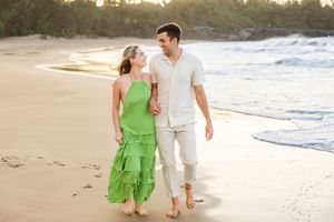 Happy couple walks hand in hand along tropical beach at golden sunset hour.