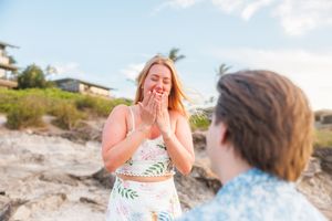 Woman covering mouth in surprise during beach proposal with man facing her in Hawaii.
