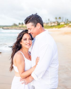 Smiling woman in white dress embraced by man on a tropical beach.