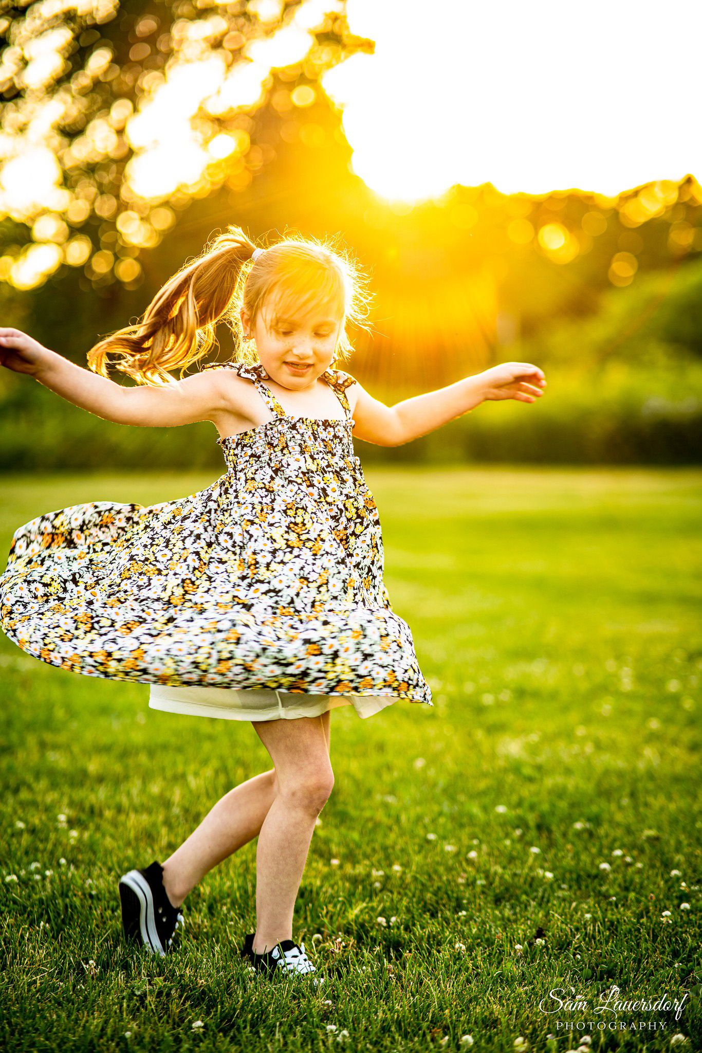 Young girl in daisy dress spinning joyfully in green park during golden sunset.