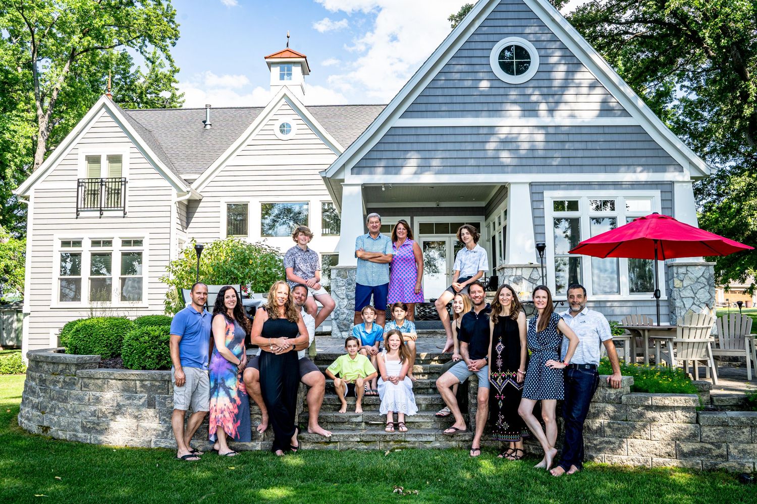 A large group gathers on the porch of a beautiful white and blue Victorian-style house. Family portrait photographer