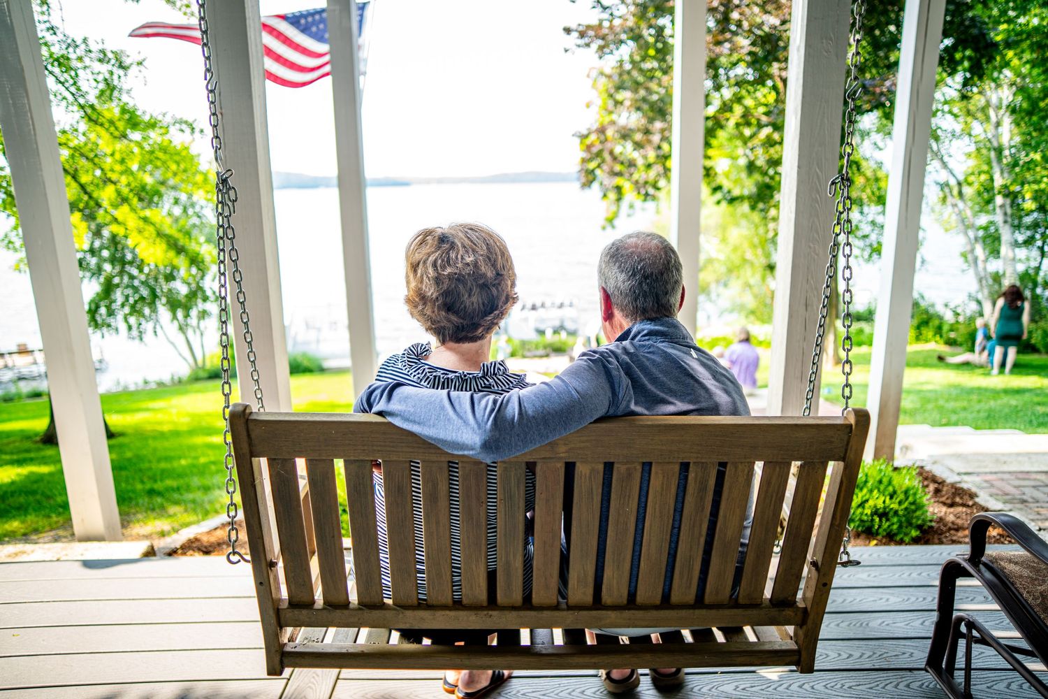 Couple sitting together on a porch swing overlooking a lakeside garden.