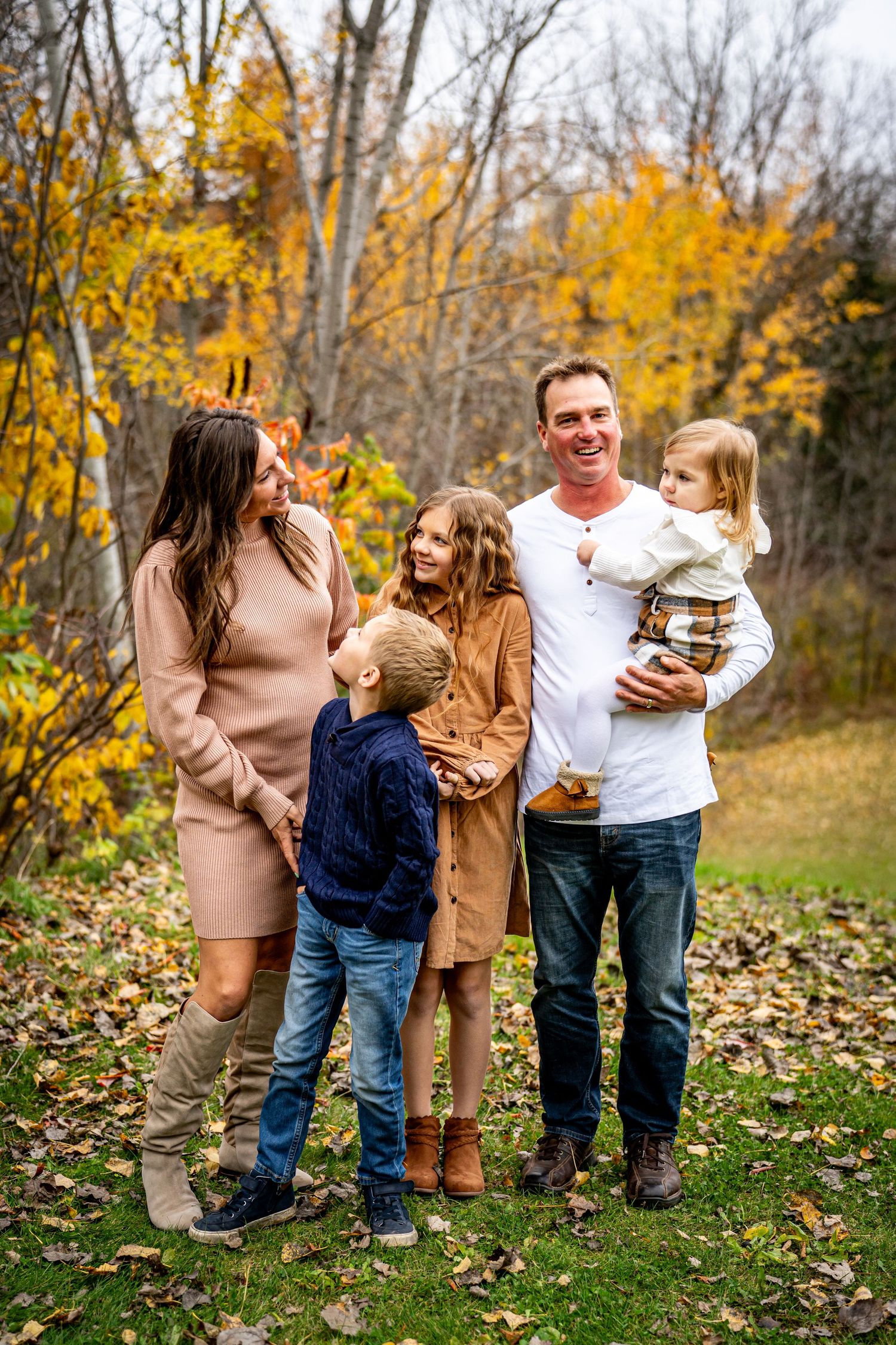 A happy family of five posing together outdoors among vibrant autumn foliage in a park setting.