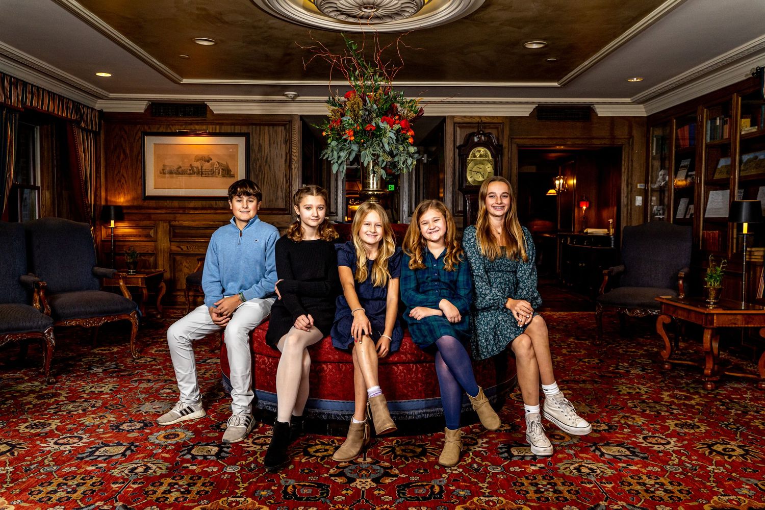 Group of four children posing together on red sofa in elegant decorated interior.