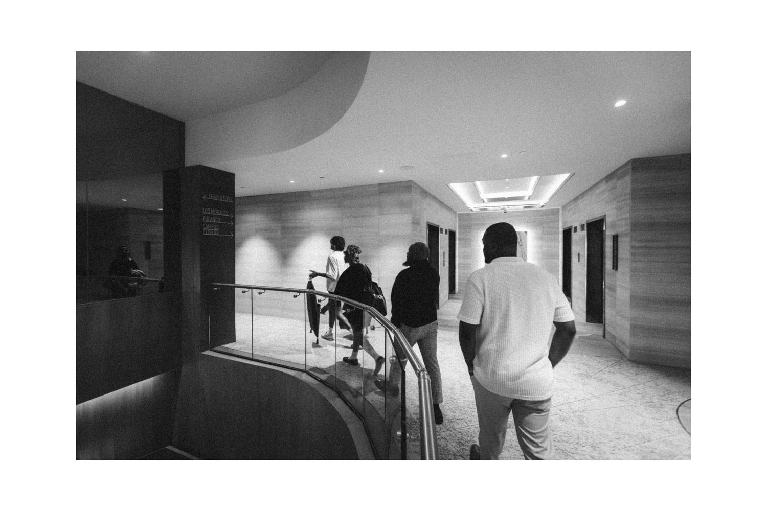 People walking through a modern hotel corridor in black and white photography.