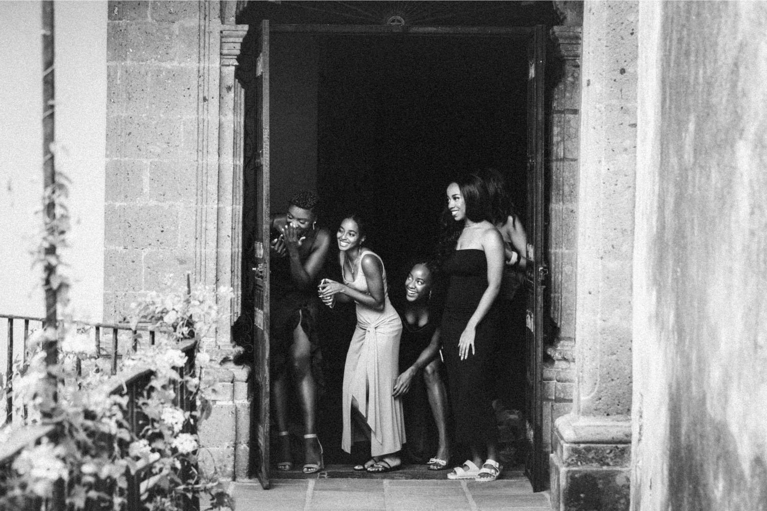 Black and white photo of a group of women standing in a doorway of a stone building, dressed in elegant attire.