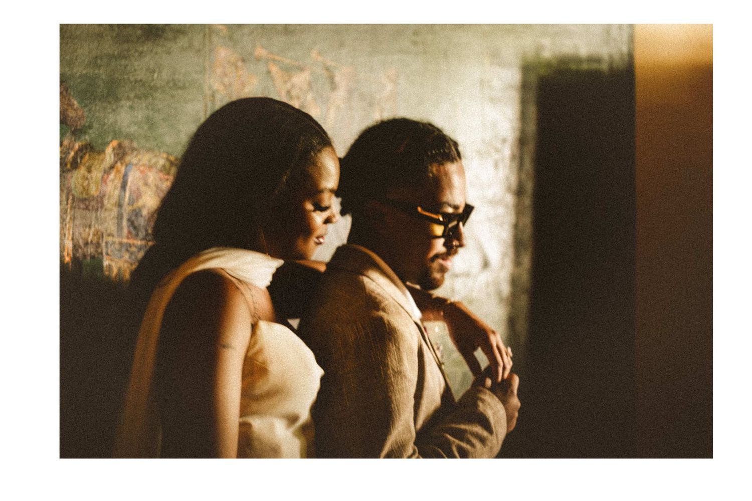 A couple shares an intimate moment, woman in white dress and man in glasses, bathed in warm golden light.