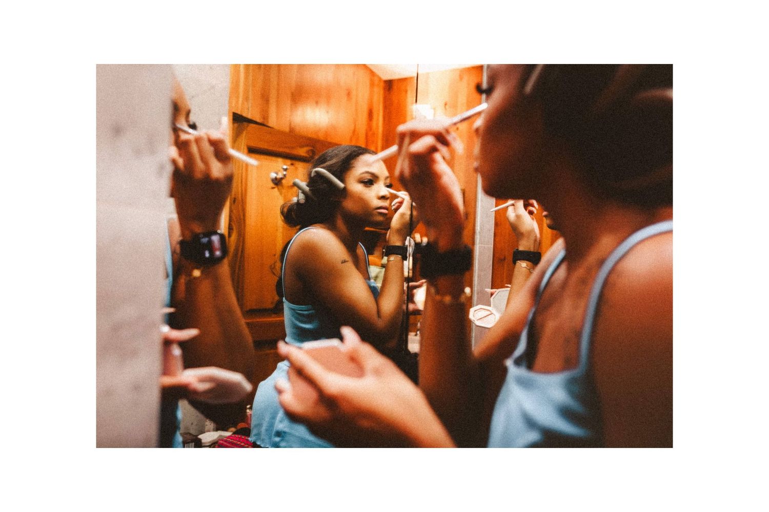 Young woman applying makeup while looking in a mirror, captured in warm tones in a cozy room.