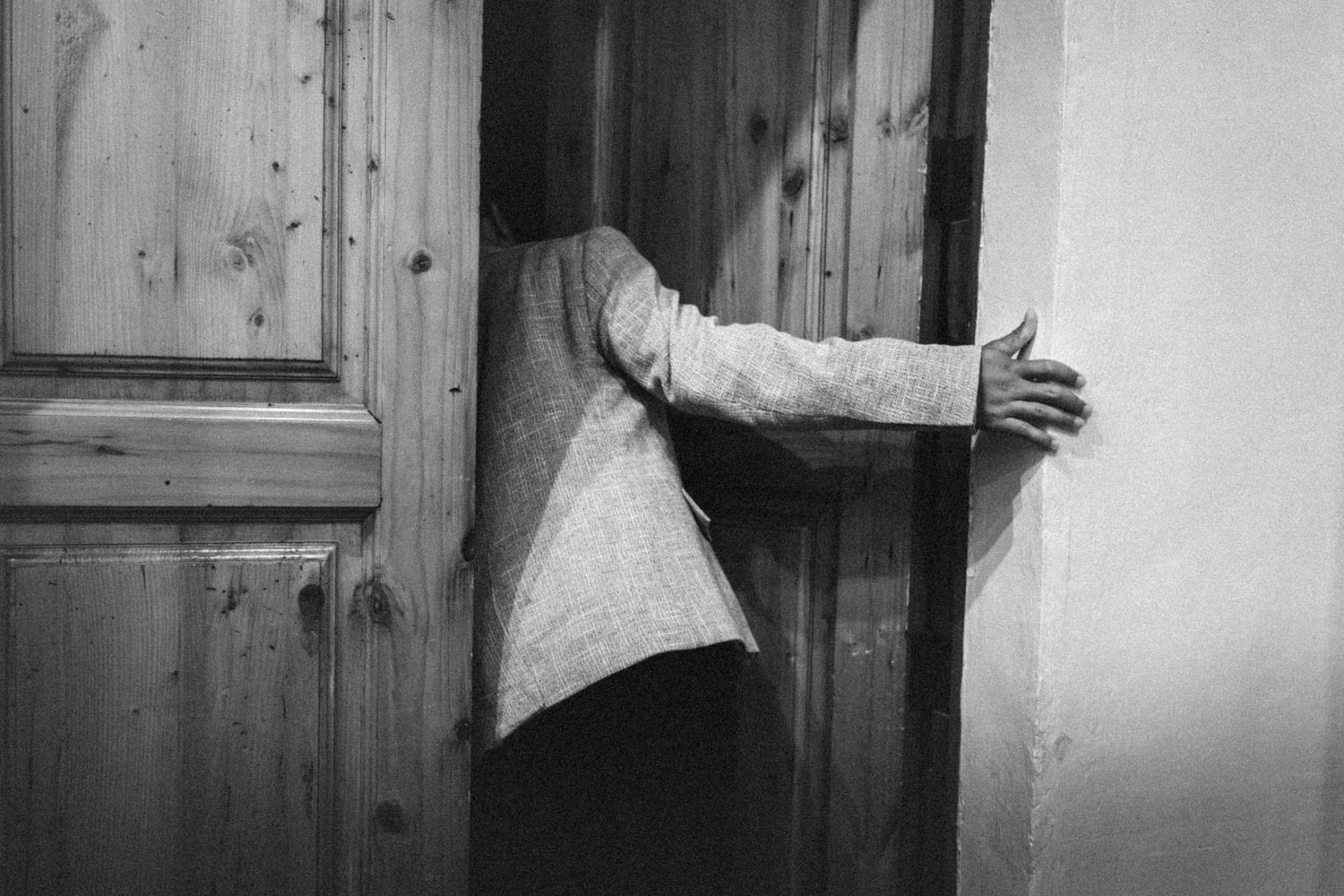 A person in a gray blazer reaches around a wooden door in a black and white fine art photograph.