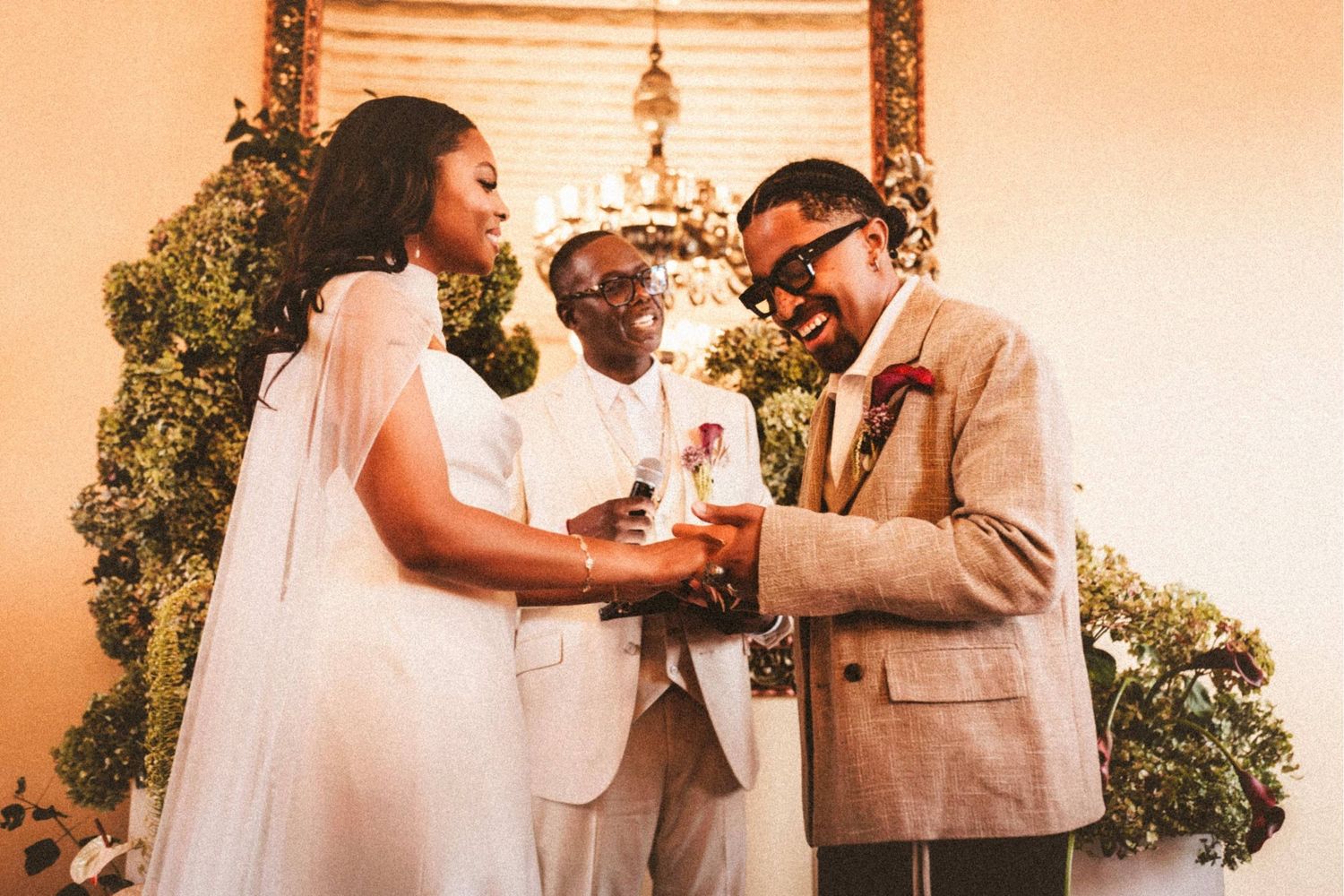 Bride and groom exchange rings during an intimate indoor wedding ceremony with floral decorations.