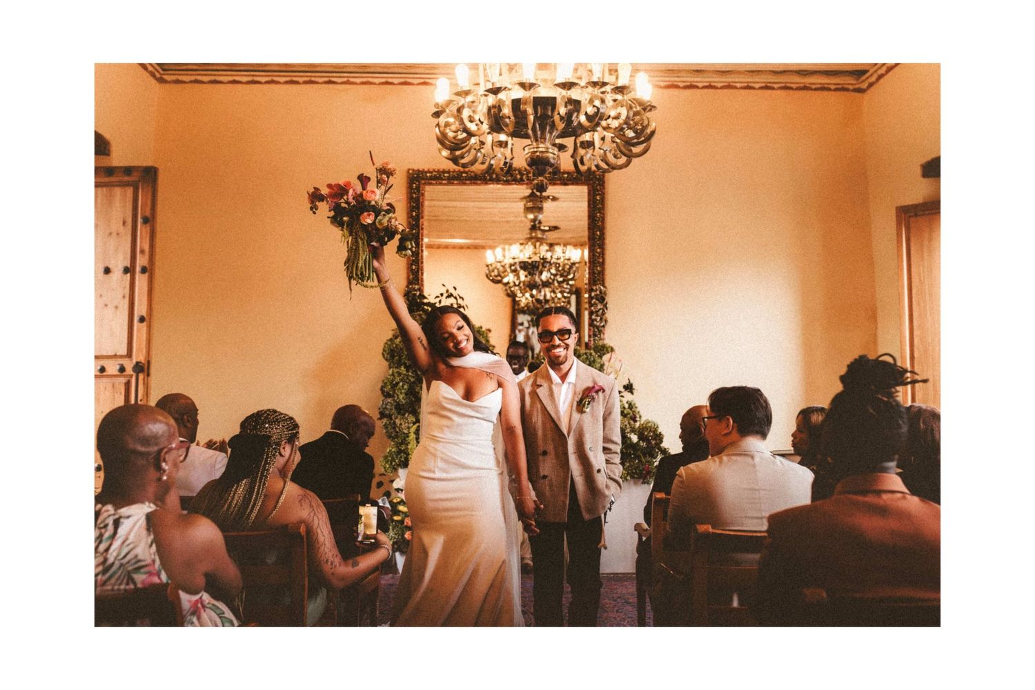 Newlyweds celebrate joyfully at their wedding ceremony under a grand chandelier.