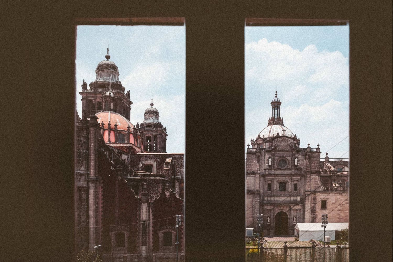 View through two windows of historic baroque cathedral domes and ornate facades in Mexico City's Zocalo plaza.