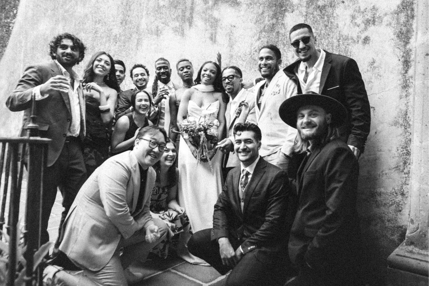 Wedding party group photo in black and white with bride and groom surrounded by guests.