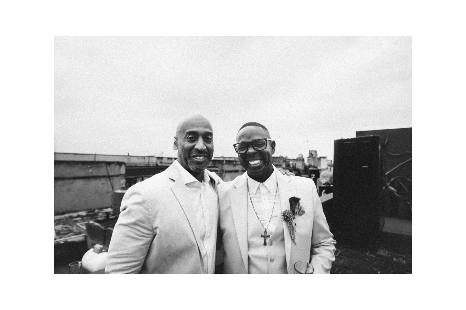 Two men in white suits smiling on rooftop in black and white photo.