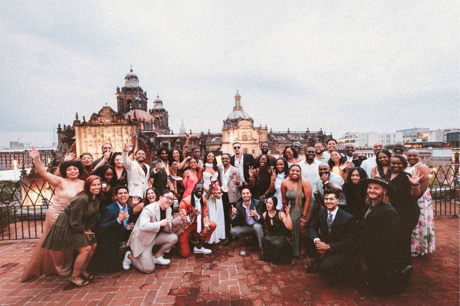 Large diverse group posing on rooftop terrace with historic European city architecture in background.