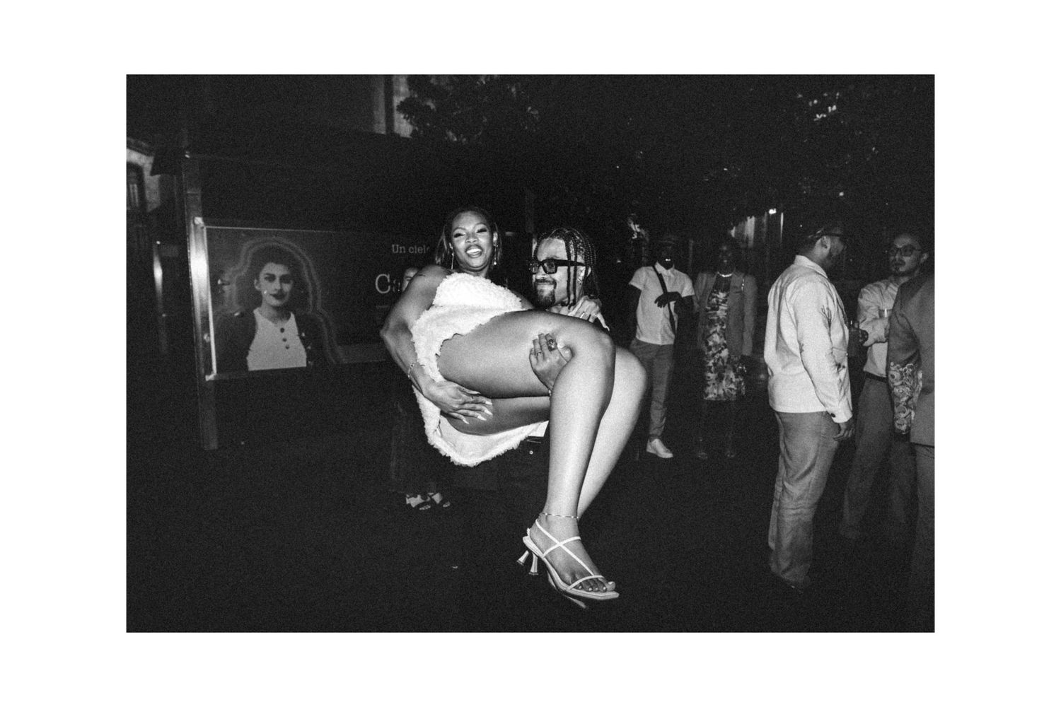Black and white photo of a woman being carried at a lively nightclub event.