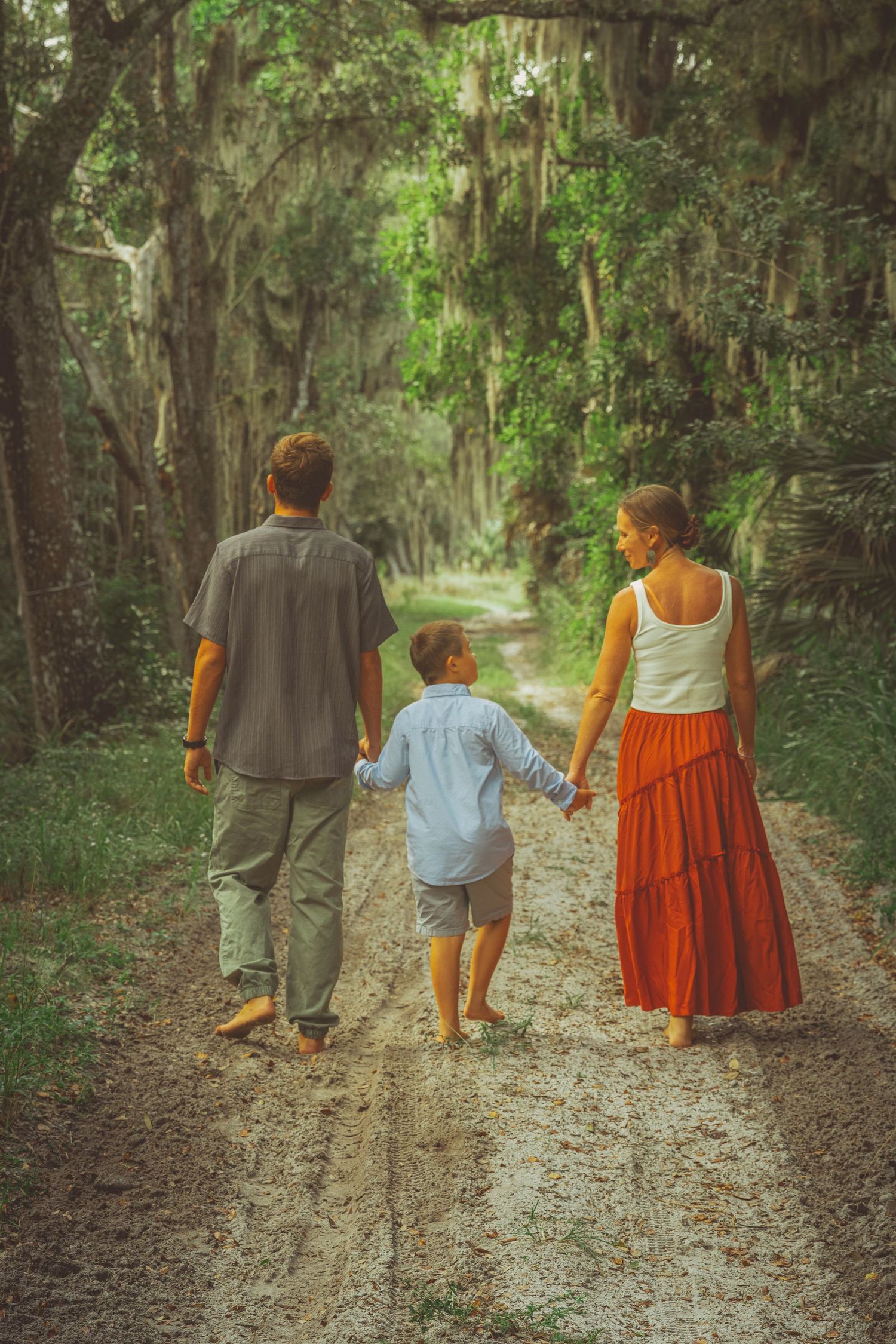 Mother and two sons walks down a path for a family photoshoot as the youngest son looks up into his mother's eyes near White City, Florida.