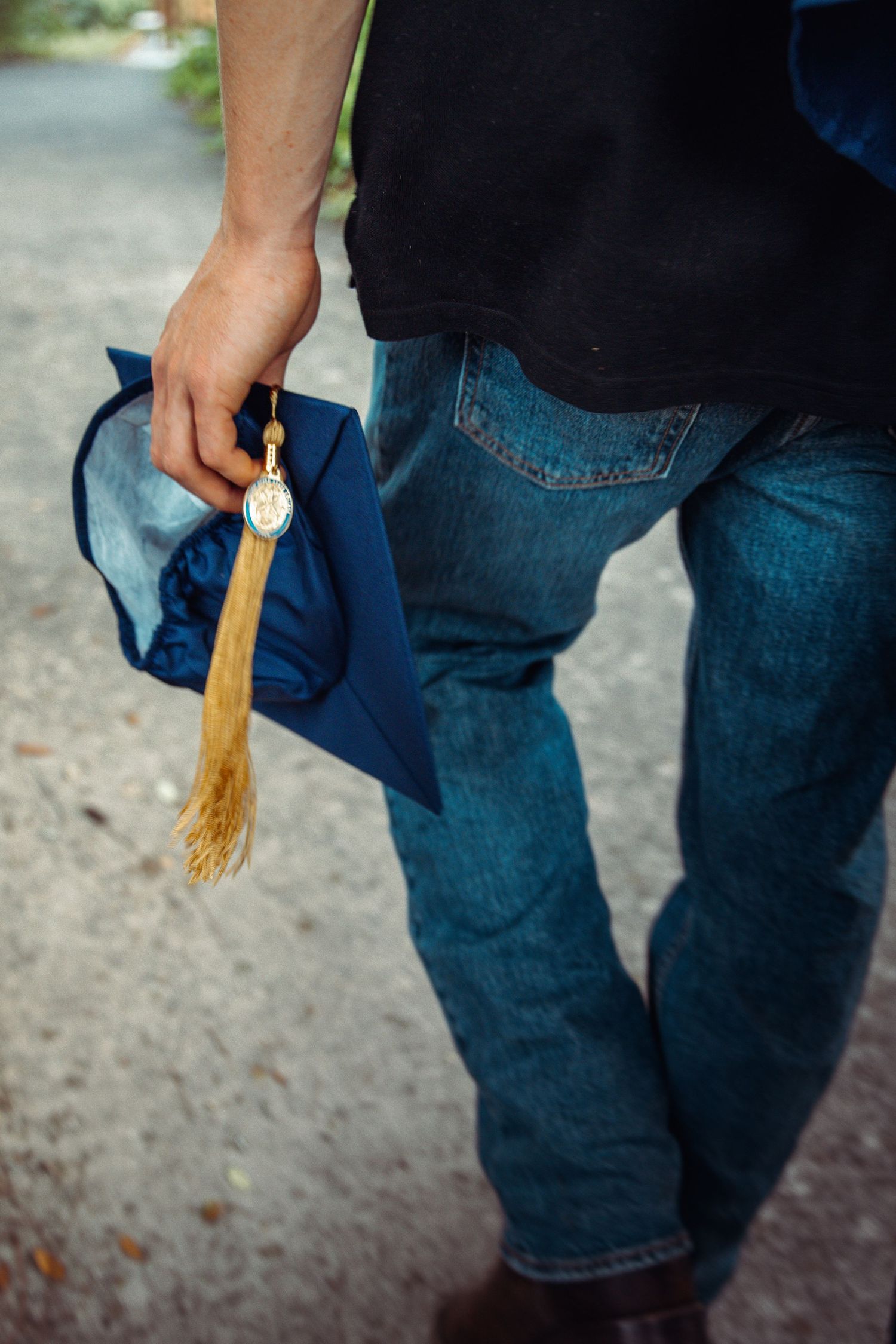 Graduation photo detail image of cap with tassel and man walking in jeans on a trail in Fort Pierce, Florida.