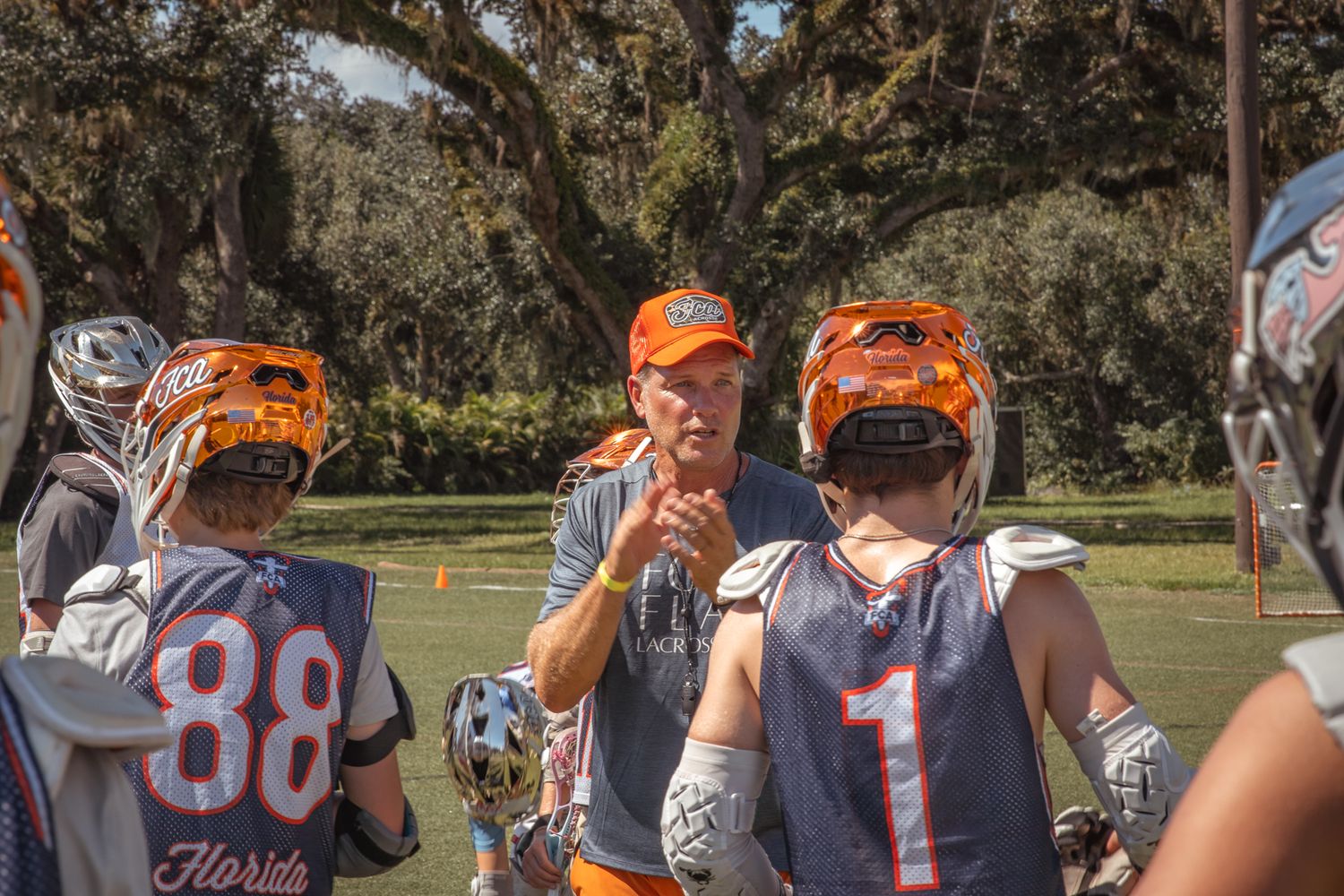 Sports Photography action shot as a lacrosse coach speaks to players on a field in the Florida sun.